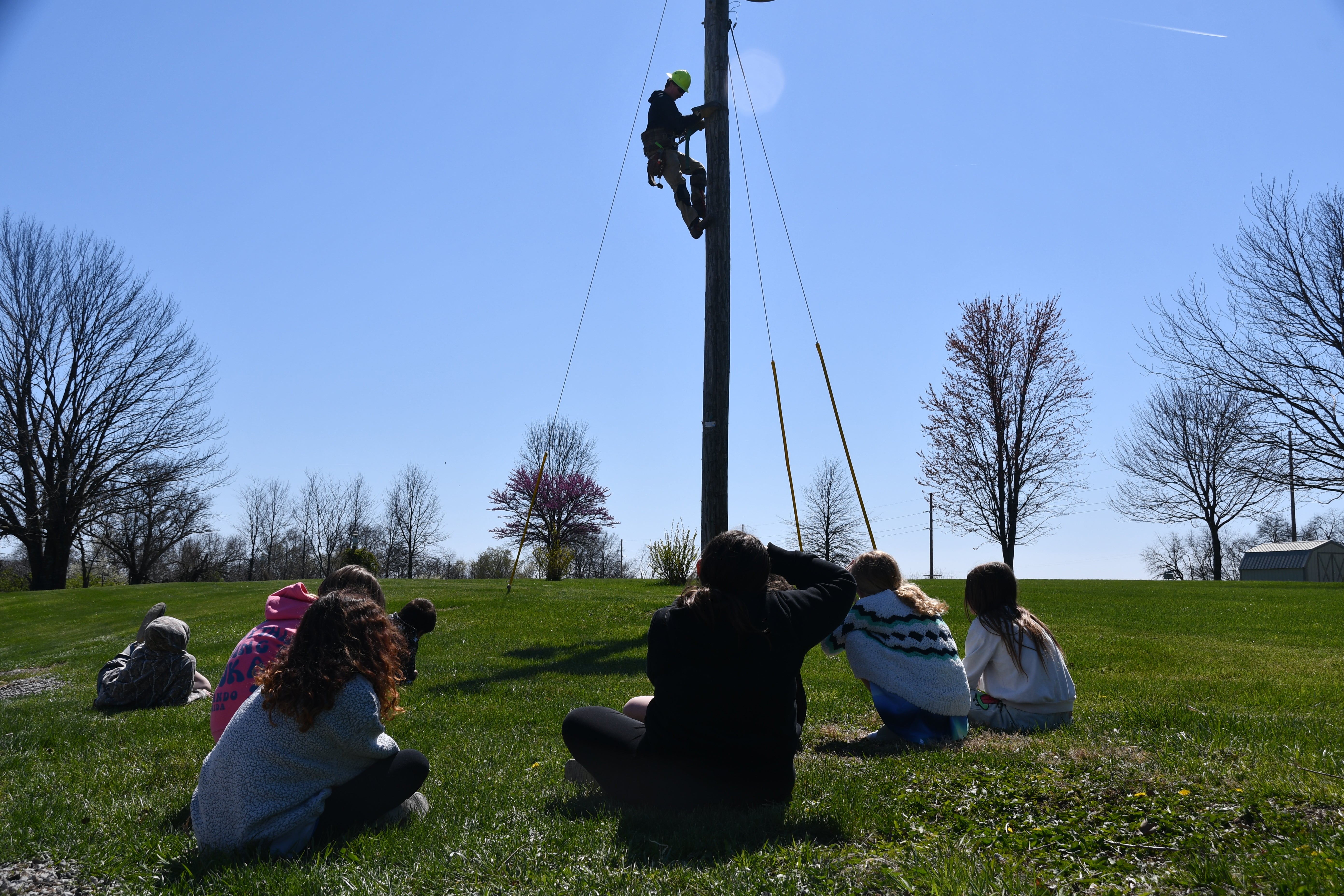 Lineman climbing a pole while students watch